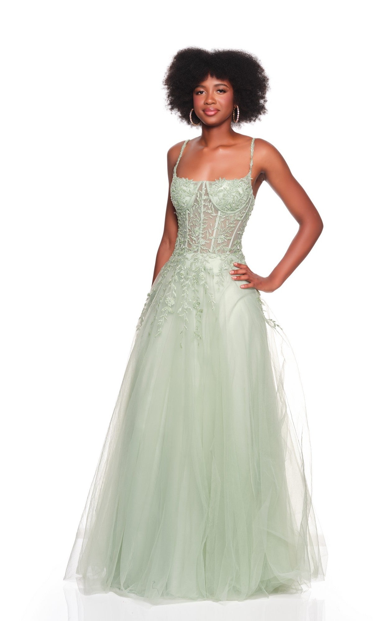 A woman poses with one hand on her hip, wearing the Dave and Johnny 12907 long prom dress in light green, featuring an embroidered bodice and a flowing A-line tulle skirt against a white backdrop.